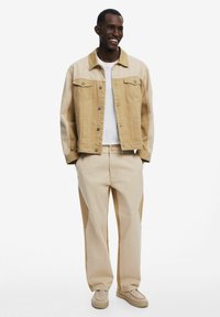 Beige denim jacket with a light tan body, silver buttons, and chest pockets, paired with matching light beige pants and beige shoes.
