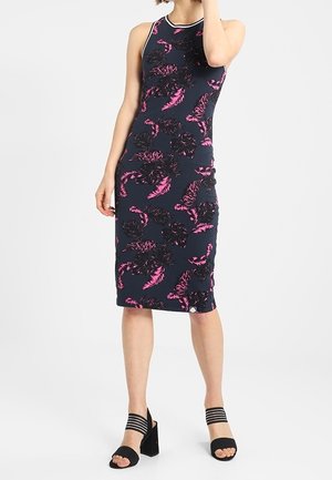 Dopasowana granatowa sukienka bez rękawów z różowo-czarnym kwiatowym wzorem, noszona z czarnymi sandałami na blokowanym obcasie z wieloma paskami.