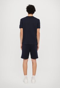 T-shirt azul marinho de manga curta e calções a condizer, feitos de tecido suave, combinados com sapatilhas brancas. Design minimalista, sem padrões visíveis.