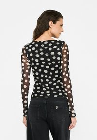 Maglietta nera a maniche lunghe con motivo a pois trasparente bianco, scollo rotondo, stile aderente. Abbinata a jeans scuri.