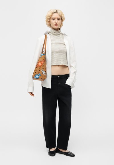 Νεαρό άτομο με κατσαρά ξανθά μαλλιά, που φοράει ριγέ crop top, άσπρο χαλαρό πουκάμισο, μαύρο παντελόνι, μαύρα παπούτσια και κρατάει μια μπεζ τσάντα ώμου με σχέδιο.