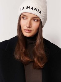 Krém színű, bordás sapka, melyen fekete hímzéssel szerepel az "LA MANIA" felirat. A modellen sötét kabát és barna felső van, hosszú barna hajjal.