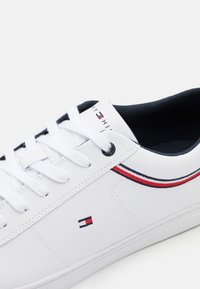 Baskets en cuir blanc avec lacets blancs, intérieur bleu marine et bandes ainsi que logo rouge, blanc et bleu sur le côté et la languette.