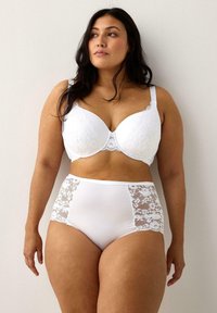 Hvid blondedragt med glatte skåle og justerbare stropper; parret med højtaljede hvide trusser med blondesidepaneler og elastisk talje.