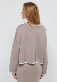 Pull court marron clair à manches longues, avec une hem et un col contrastés en blanc. Texture douce avec une coupe décontractée.