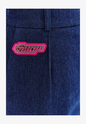 Denim z ciemnoniebieskim odcieniem ozdobiony jest wyraźną różową łatą z logo "The Powerpuff Girls", co dodaje zabawnego akcentu.