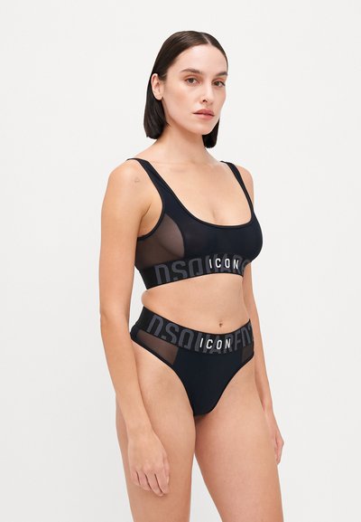 Černá souprava spodního prádla se střihovým braletem s výstřihem ve tvaru lodičky a síťovými panely, která má logo pás. Odpovídající kalhotky mají elastický pás.