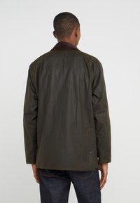 Olive green jacket with a brown corduroy collar, straight cut, two side pockets, and buttoned cuffs, made from a lightweight, water-resistant material.