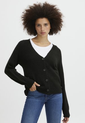 Schwarze Strickjacke mit V-Ausschnitt, langen Ärmeln und sechs Knöpfen auf der Vorderseite. Weiche Textur, kombiniert mit einem weißen Hemd darunter.