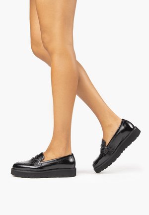Mocassins noirs brillants avec une semelle plateforme épaisse, ornés de clous décoratifs sur le bout et d'une texture en cuir lisse.