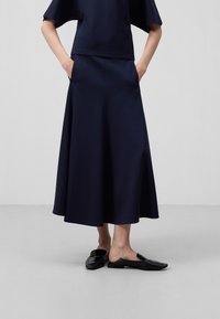 jupe mi-longue fluide bleu marine avec une taille structurée et des poches latérales, associée à des chaussures noires à enfiler élégantes. Texture de tissu lisse.