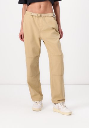 Beige high-waist pants with built-in belt worn with white sneakers and a cropped black top, shown from waist to feet.
