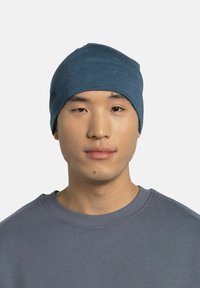 Blue knit beanie made of soft material, features a smooth texture and snug fit. Worn by a person in a gray sweatshirt.