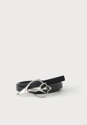 Ceinture en cuir noir avec une boucle métallique argentée abstraite en forme d'une forme organique ouverte, présentée enroulée sur une surface blanche.