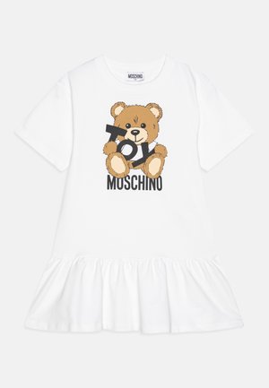 Hvid kortærmet kjole med flæsekant, med en bamse, der holder bogstaver, der staver "TOY", og mærkenavnet "Moschino" nedenunder.