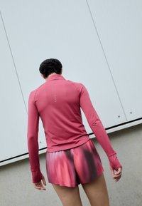 Langarmige, roze sporttop met een kraag, gecombineerd met geplooide shorts met een gradientpatroon van roze naar donkerrood.
