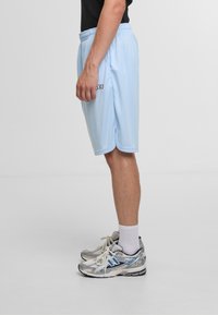 Lyseblå træningsshorts med elastisk talje og sideskår, parret med grå og blå sportsko og hvide ankelstrømper.
