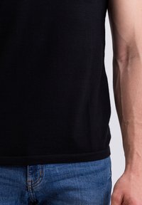 Černý pletený bezrukávový top s kulatým výstřihem, který má hladkou texturu. V kombinaci s modrými džíny z denimu s jemným švem.