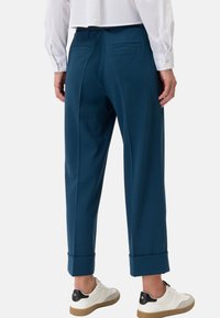 Teal broek met een ontspannen pasvorm, voorzien van opgerolde manchetten, een soepele textuur en twee achterzakken, gecombineerd met witte sneakers.