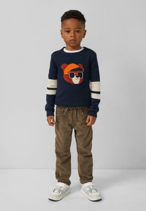 Marinefarbener Pullover mit einem Tiermotiv und weißen Streifen. Strukturierte braune Cordhosen. Weiße Sneakers mit grauen Akzenten.