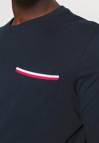 Mörkblå långärmad skjorta med en bröstficka som har röda, vita och mörkblå randiga detaljer. Mjuk bomullstyg med rundad halsringning.