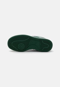 Suola di scarpa verde con un motivo testurizzato e accenti circolari. Presenta profonde scanalature per la trazione e un'area tallonata ben definita per la stabilità.