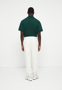 Grøn polo skjorte og hvide joggere med elastisk talje, set fra ryggen. Sneakers med grå accenter fuldender outfittet.