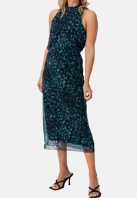 Robe midi à imprimé léopard en bleu sarcelle et noir, avec un col licou et un tissu fluide et transparent. Mise en valeur par un corsage ajusté et une jupe ample.