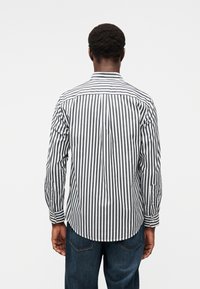 Πουκάμισο με μακριά μανίκια που διαθέτει κάθετες ρίγες σε μαύρο και άσπρο, γιακά με κουμπιά και στρογγυλεμένο τελείωμα. Το ύφασμα φαίνεται λείο και λεπτομερειακά υφασμένο.