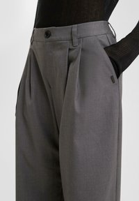 Grijze op maat gemaakte broek, gemaakt van gladde stof, heeft plooien en een knoopsluiting bij de tailleband. Inclusief zijzakken.