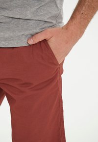 Mörkröda shorts gjorda av mjukt tyg, med sidofickor och en avslappnad passform. Midjebandet är delvis täckt av en grå topp.