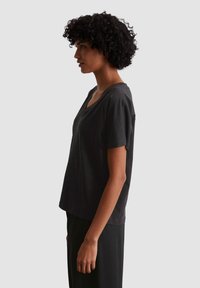 Zwarte V-hals T-shirt met korte mouwen, met een relaxte pasvorm en zachte textuur, zijaanzicht tegen een neutrale achtergrond.