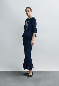 Top peplum bleumarin cu material texturat și mâneci trei sferturi, asortat cu o fustă evazată. Pantofi negri fără toc și un colier cu straturi.