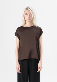 Brown short-sleeve top with a loose fit and rounded neckline, made from smooth fabric. Features rolled sleeves and subtle side seam details.