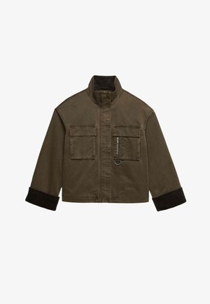 Veste courte marron avec col montant, deux poches à rabat sur le devant, détail zippé sur la poche droite et manches noires avec poignets retroussés.