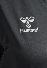 Svart atletiskt tyg med en vit Hummel-logotyp som visar en bi-design med geometriska accenter och en mjuk textur.