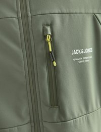 Groene jas met een gladde textuur, voorzien van een ritszak met een gele trekknop. "JACK & JONES" logo in het wit gedrukt.