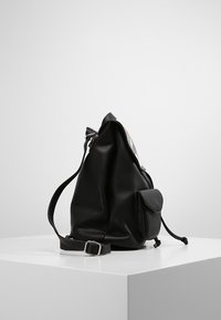 Svart läderryggsäck med texturerad yta, försedd med sidoficka och justerbar rem. Minimalistisk design med en avslappnad form.