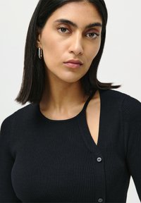Top negru din tricot cu dungi, cu mâneci lungi, având o decupare unică pe un umăr și detalii subtile cu nasturi pe partea din față.