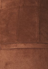 Bruin suède stof met een zachte textuur, met een naaddetail en een glad accent langs de rand. Geen patronen of extra sluitingen zichtbaar.