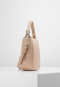 Beige texturovaná kožená taška s nastavitelným popruhem, stříbrnými kovovými doplňky a malým zlatým logem ležící na bílém podstavci na neutrálním pozadí.