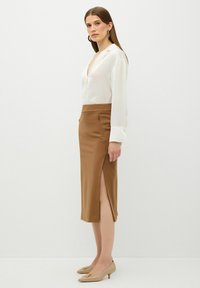Witte blouse met een diepe V-hals en lange mouwen. Bruine getailleerde rok met zijsplitten. Beigekleurige hakken met decoratieve accenten.
