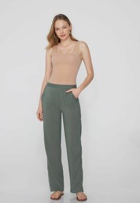 Top incrociato beige con scollatura quadrata, abbinato a pantaloni larghi verde-grigi con tasche laterali e una texture liscia.