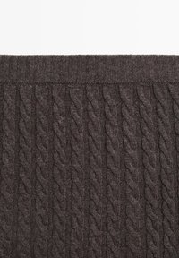 Dunkelbraunes Strickgewebe mit einem Zopfmuster aus erhabenen, verdrehten Designs. Die Textur ist weich und entlang des oberen Randes gerippt.