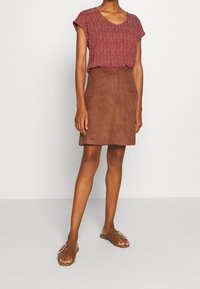 Rød mønstret top med korte ærmer og en brun ruskinds mini nederdel. Båret med flade brune sandaler. Enkel, afslappet tøjdesign.