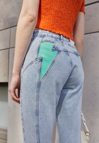 Calças de ganga azul claro com um emblema de relâmpago verde no bolso de trás. O tecido tem uma textura suave e um design padrão de cinco bolsos.