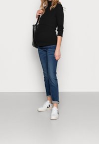 Svart långärmad topp, figurnära under bysten; blå jeans, slim fit, uppvikta ärmslut; vita sneakers med svarta detaljer; svart tote-väska.