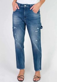 Jean en denim bleu délavé avec une coupe décontractée, présentant des détails usés, cinq poches et une coupe droite.