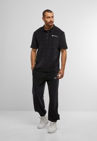 Black terry polo and pants set with a textured diamond pattern. Collar and logo accents, paired with white sneakers.