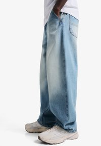 Svetlo modre široke kavbojke z izpranim videzom in velikimi žepi, kombinirane z bež športnimi čevlji.